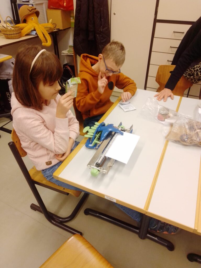 Zwei Schüler sitzen am Tisch und arbeiten mit einer Braille-Schreibmaschine.