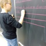 Ein Schüler notiert eine Spielidee mit Kreide an der Tafel.