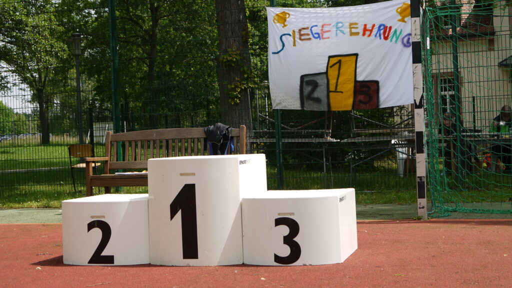 Das Bild zeigt ein leeres Siegerpodest. Im Hintergrund hängt ein Laken mit der Aufschrift "Siegerehrung" am Zaun
