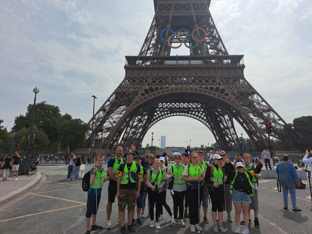 Gruppenfoto vor dem Eiffelturm. Am Eiffelturm sind die olympischen Ringe angebracht.