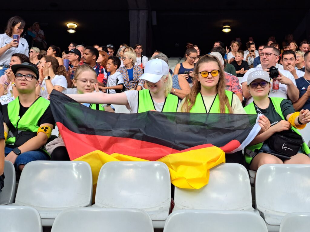 Schülerinnen und Schüler sitzen im Stadion und halten eine große Deutschland-Fahne in ihren Händen.