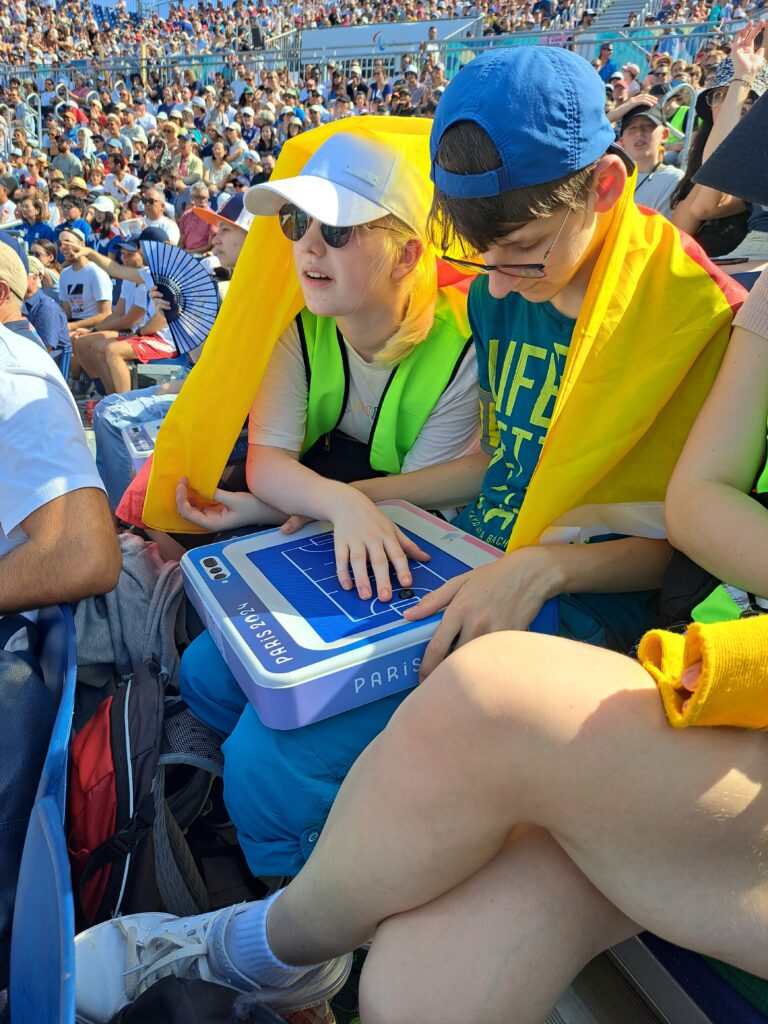 Zwei Schüler verfolgen mithilfe eines Visionpads das Geschehen auf dem Spielfeld von der Zuschauertribüne aus