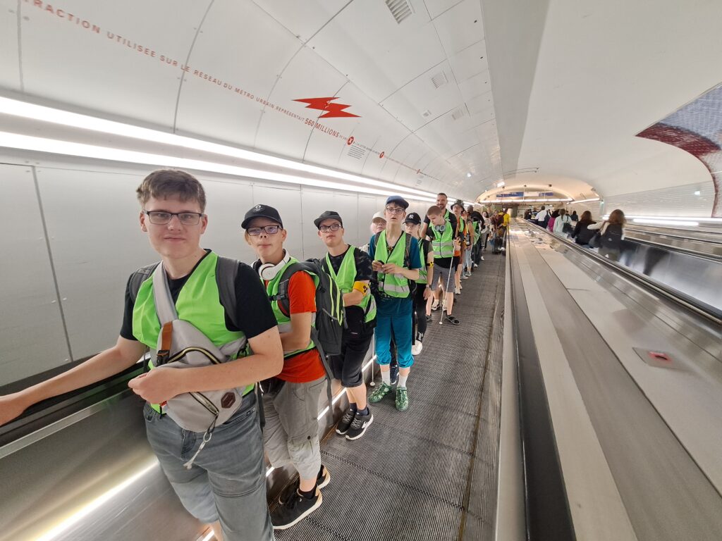 Die Schüler stehen aufgereiht auf einem Rollband in einer Metrostation