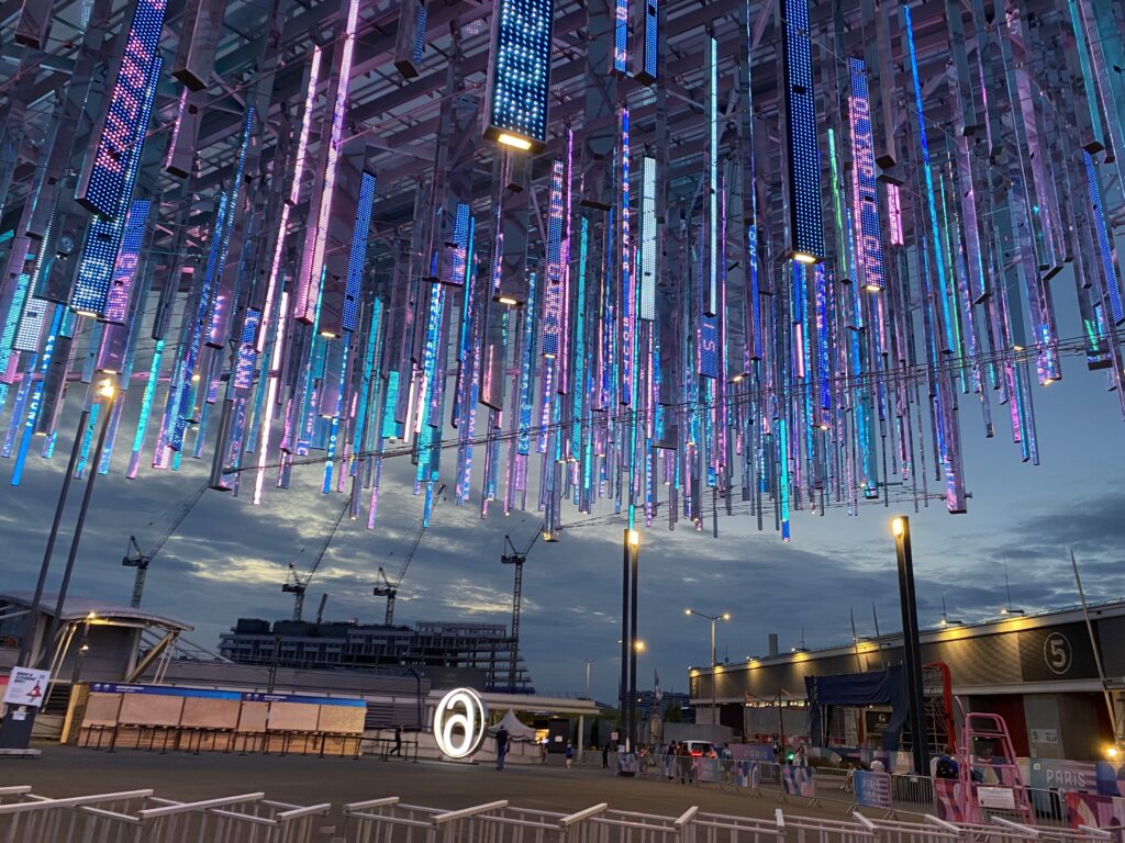 Eine Installation von hunderten kleinen Display hängt von der Decke einer Veranstaltungshalle. Auf den Displays erscheinen Botschaften in französischer Sprache.